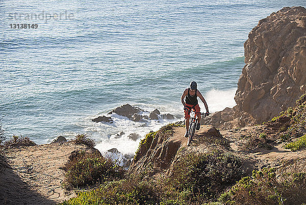 Männlicher Athlet beim Fahrradfahren auf Felsen am Meer