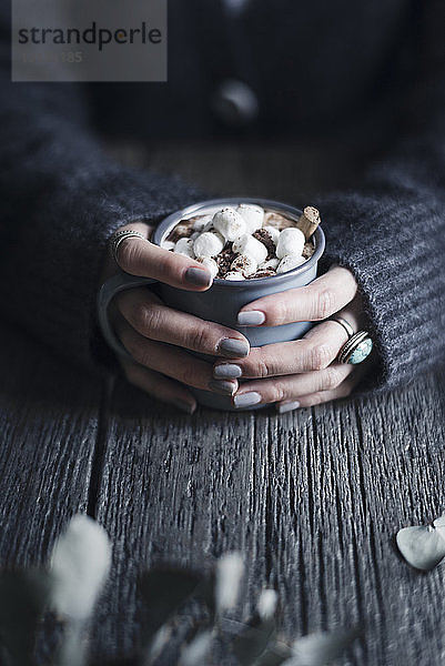 Ausgeschnittenes Bild einer Frau  die einen Becher mit heißer Schokolade und Marshmallows an einem Holztisch hält