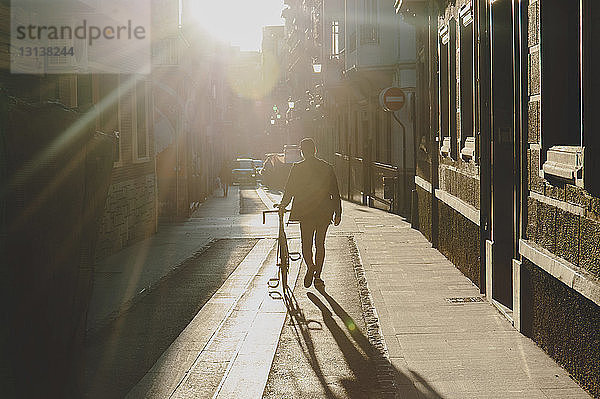 Rückansicht eines Mannes  der bei Sonnenuntergang mit dem Fahrrad auf einem Fußweg geht