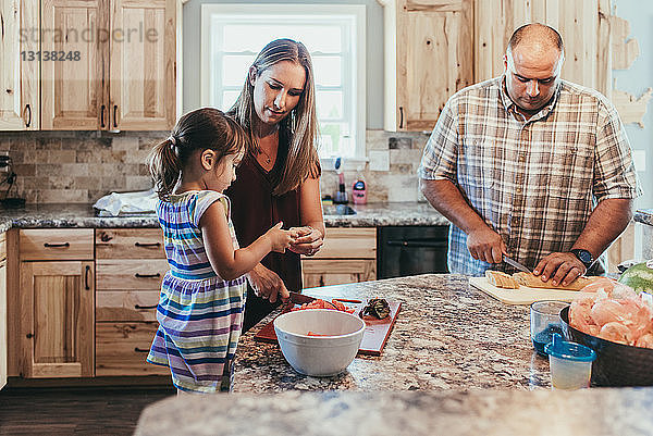 Eltern bereiten das Essen vor  während sie mit der Tochter zu Hause in der Küche stehen
