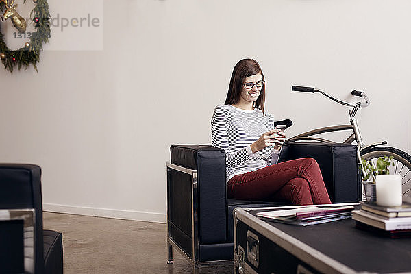 Lächelnde Geschäftsfrau benutzt Telefon  während sie im Büro sitzt