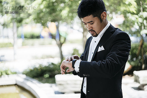 Junger Geschäftsmann kontrolliert die Zeit auf einer intelligenten Uhr in der Stadt