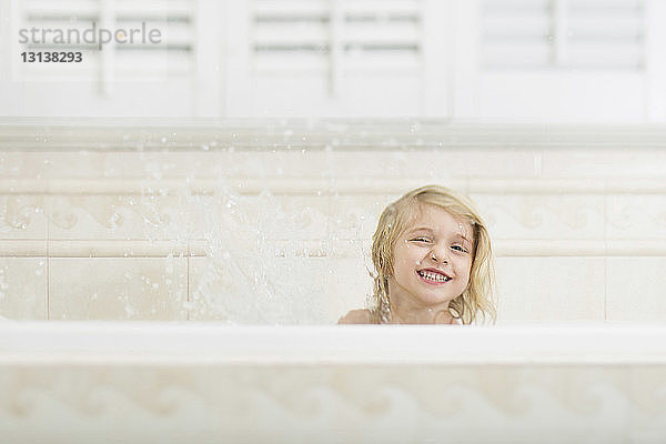 Fröhliches Mädchen  das zu Hause beim Baden in der Badewanne Wasser spritzt