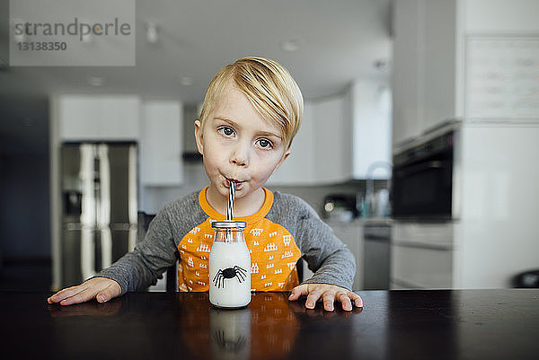 Junge trinkt Milch  während er am Tisch sitzt