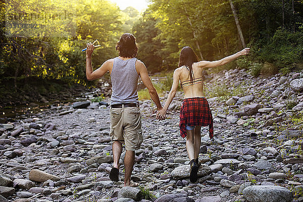 Rückansicht eines Paares  das sich beim Gehen auf Felsen im Wald an den Händen hält