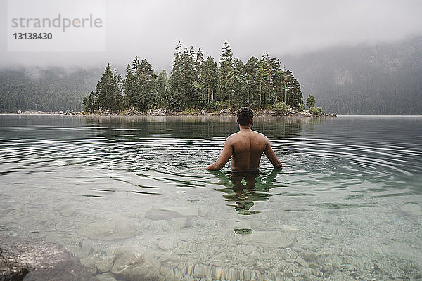 Mann ohne Hemd schwimmt im See am Wald
