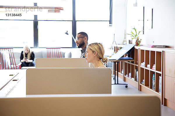 Seitenansicht von Geschäftsleuten  die wegschauen  während sie im Büro an Schreibtischen sitzen