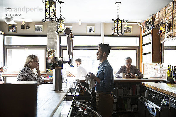Lächelnder Besitzer im Gespräch mit Kunden  während er an der Theke im Café steht