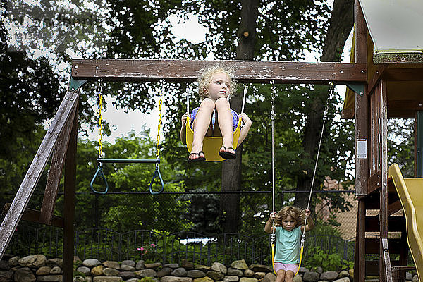 Süße Schwestern schaukeln auf Schaukeln gegen Bäume auf dem Spielplatz