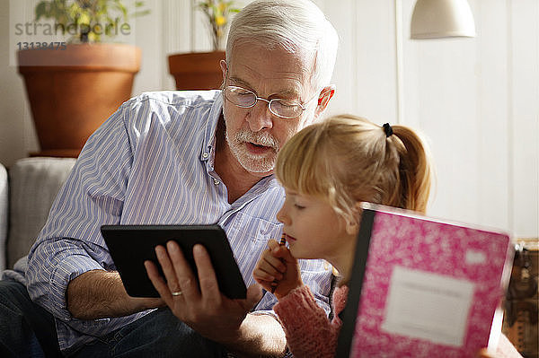Großvater zeigt Enkelin Tablet-Computer beim Lernen zu Hause