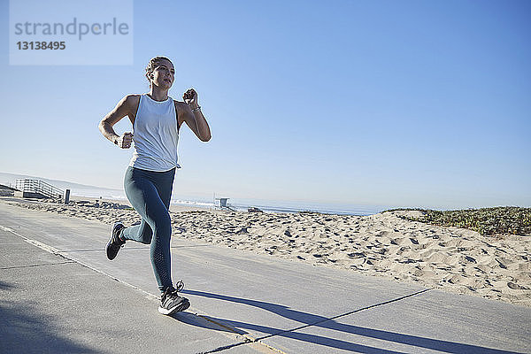 Frau in voller Länge joggt auf der Straße am Strand vor klarem Himmel