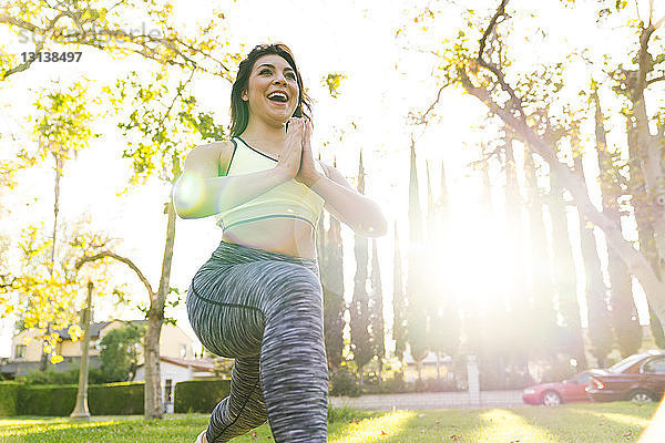 Niedrigwinkelansicht einer fröhlichen Frau  die Yoga praktiziert  während sie an einem sonnigen Tag im Park trainiert