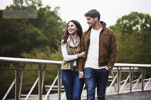 Glückliches Paar hält sich beim Gehen auf der Brücke bei klarem Himmel an den Händen