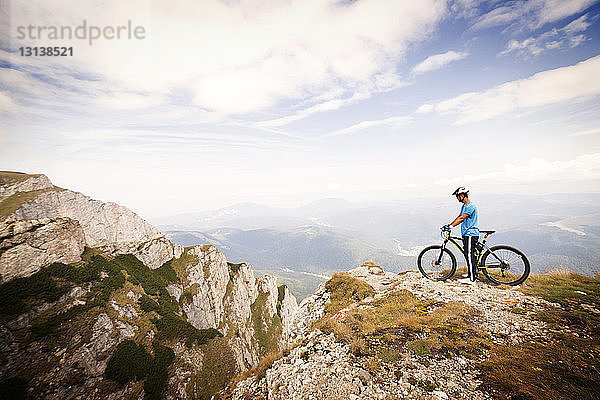 Seitenansicht eines Mountainbikers mit Fahrrad vor bewölktem Himmel