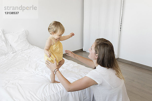 Hochwinkelansicht einer glücklichen Mutter  die ihre Tochter zu Hause im Bett laufen sieht