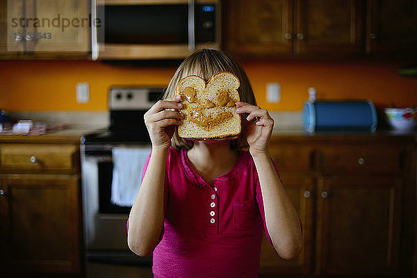 Mädchen hält sich in der Küche Brot ans Gesicht
