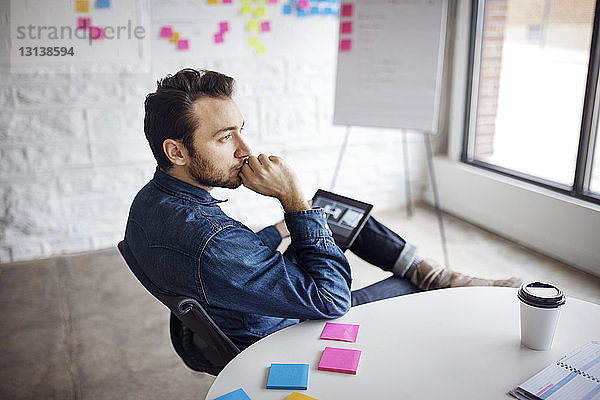 Nachdenklicher Geschäftsmann benutzt Tablet  während er im Kreativbüro sitzt