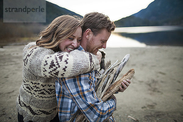 Fröhliche Freundin umarmt im Silver Lake Provincial Park ihren Freund  der Brennholz trägt
