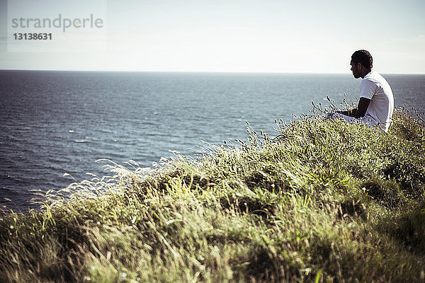 Seitenansicht eines Mannes  der auf einem Feld am See sitzt