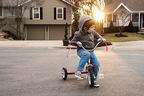 Junge trägt Kapuzenjacke  während er auf einem Dreirad sitzt