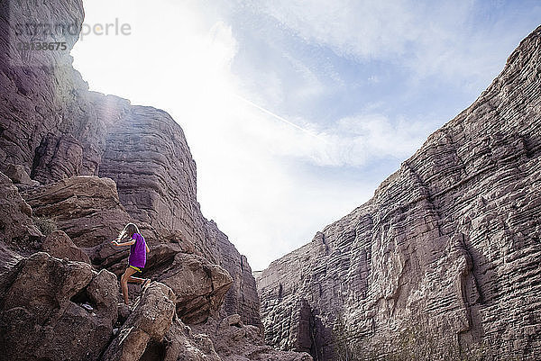 Niedrigwinkelansicht eines Mädchens beim Klettern an Felsformationen gegen den Himmel während eines sonnigen Tages