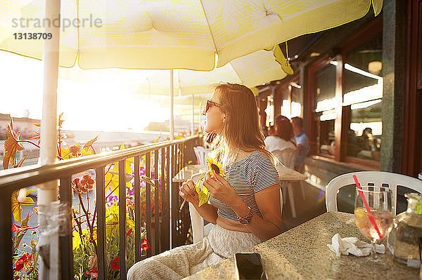 Frau mit Sonnenbrille hält Sonnenblume im Café