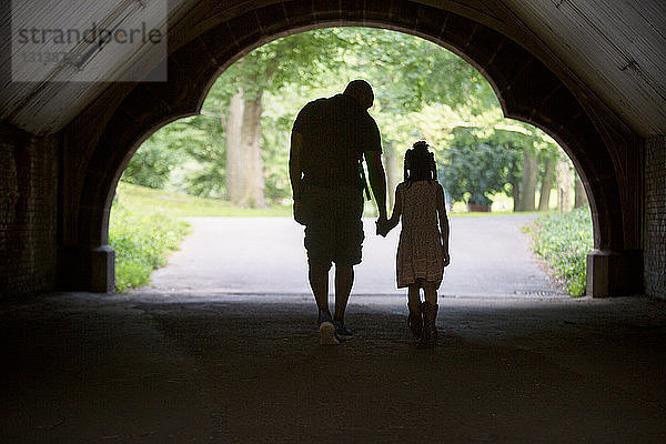 Rückansicht von Vater und Tochter  die sich an den Händen halten und im Tunnel gehen