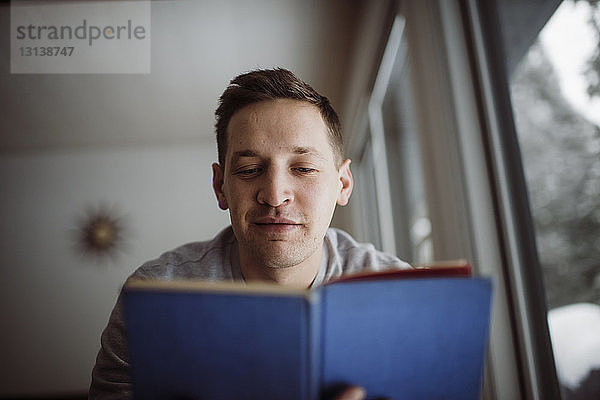 Niedrigwinkelansicht eines Mannes  der zu Hause am Fenster sitzt und ein Buch liest