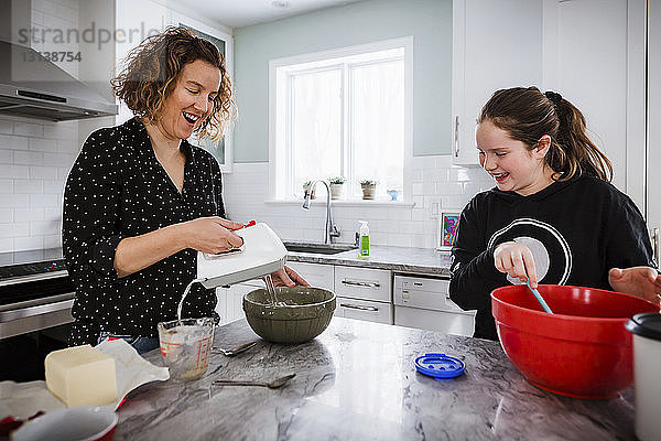 Mutter mit Tochter mischt zu Hause auf einer Kücheninsel Teig in Schüsseln