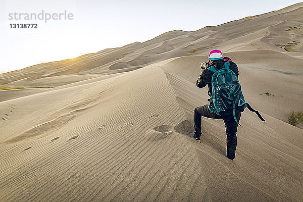 Rückansicht eines Wanderers mit Rucksack beim Fotografieren im Great Sand Dunes National Park