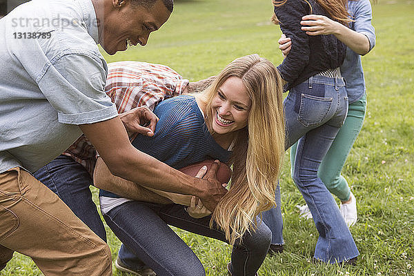 Männliche Freunde schnappen einer Frau auf einem Rasenplatz einen Fussball weg