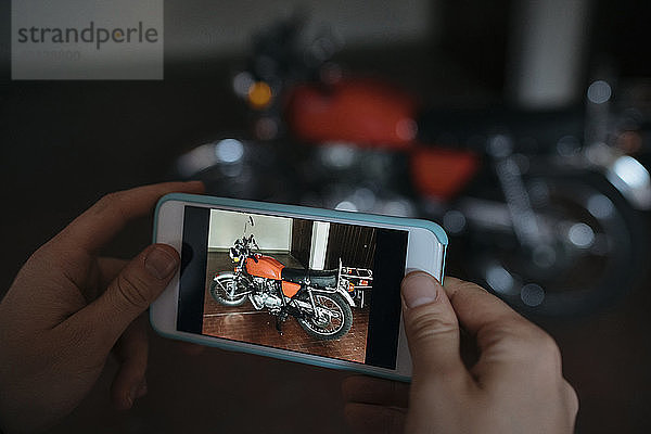 Ausgeschnittene Hände einer Frau  die in der Werkstatt ein Motorrad fotografiert