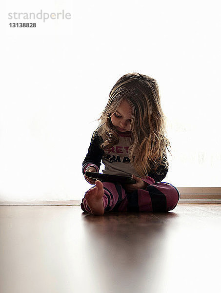 Mädchen benutzt einen Tablet-Computer  während sie zu Hause am Boden vor einem Vorhang sitzt