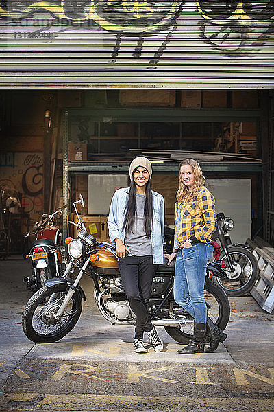 Porträt von glücklichen Besitzerinnen  die mit dem Fahrrad vor einer Autowerkstatt stehen