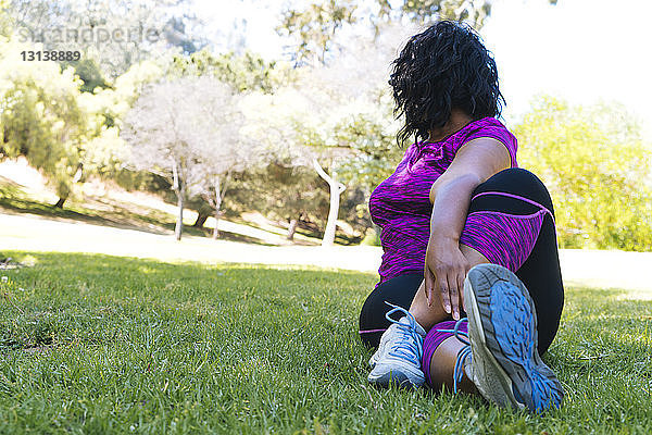 Frau  die im Park sitzend die Beine streckt