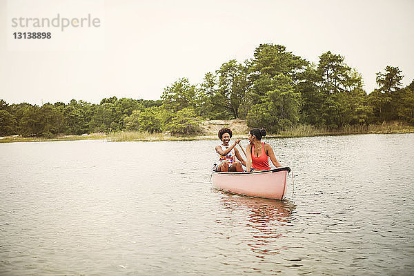 Glückliche Freunde rudern Boot auf dem See gegen den Himmel