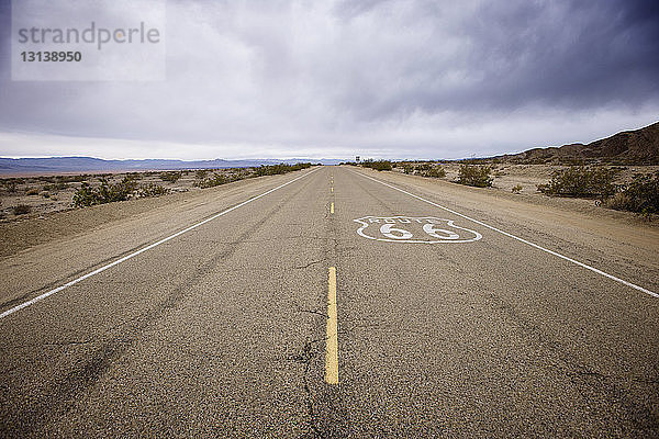 Route 66-Schild auf Wüstenstraße gegen bewölkten Himmel