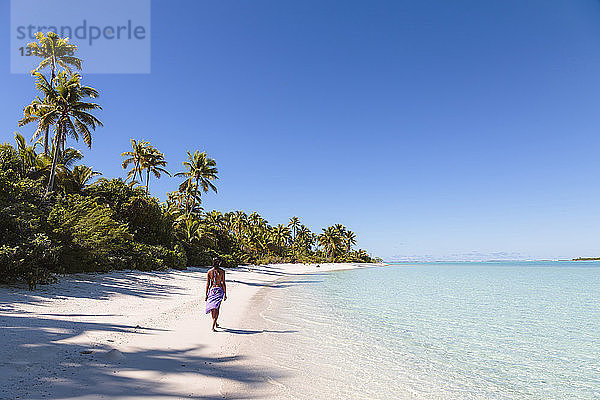 Rückansicht einer Frau  die am Strand bei strahlend blauem Himmel an einem sonnigen Tag am Strand spazieren geht