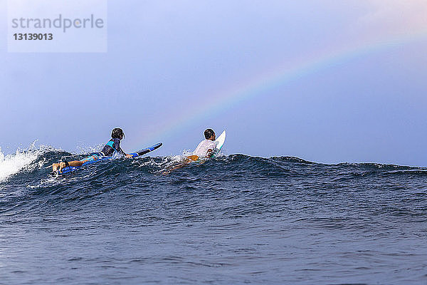 Freunde surfen auf dem Meer gegen den Himmel