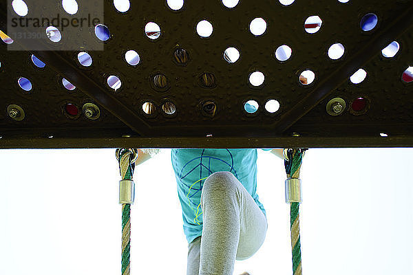 Niedrigwinkelansicht eines Mädchens  das beim Klettern auf der Strickleiter auf dem Spielplatz durch das Loch schaut