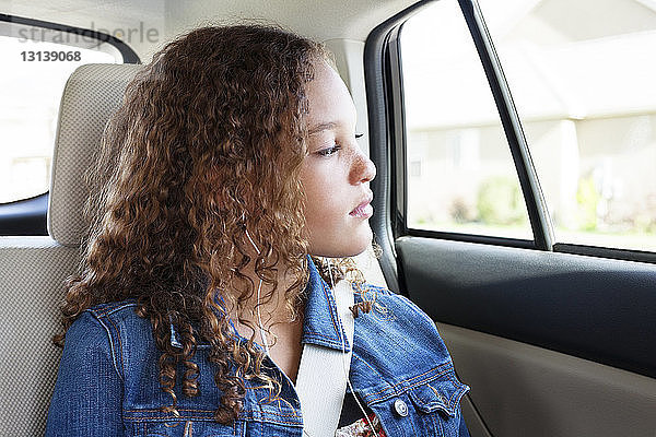 Teenager schaut durch Fenster  während er im Auto Musik hört