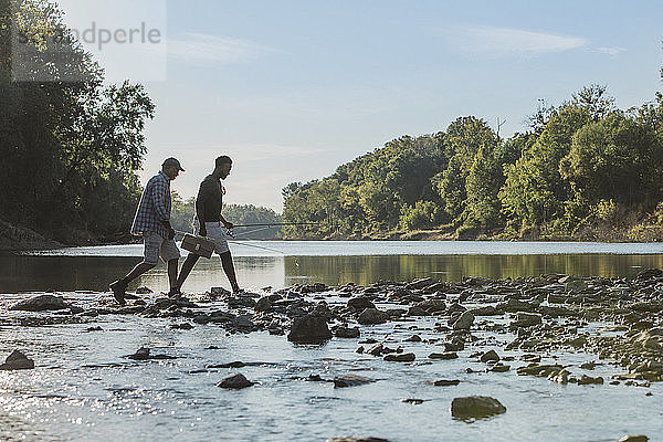 Seitenansicht von männlichen Freunden mit Angelruten  die auf Felsen im See gehen