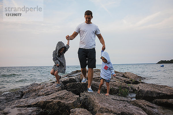 Vater und Kinder gehen auf Felsen am Meer gegen den Himmel