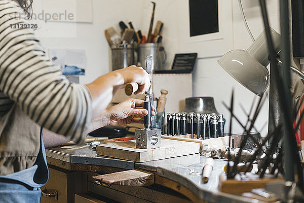 Mittelteil eines Handwerkers  der mit Handwerkzeugen arbeitet  während er in einer Werkstatt Schmuck auf dem Tisch herstellt