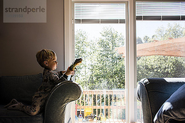 Junge spielt mit Spielzeug  während er zu Hause auf einem Sessel kniend sitzt