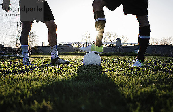 Ein niedriger Teil männlicher Freunde spielt Fußball auf einem Rasenfeld gegen den klaren Himmel im Park