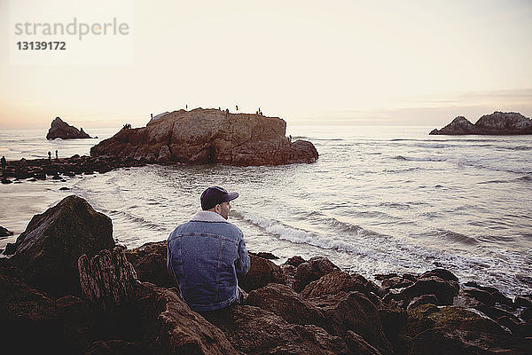 Rückansicht eines Menschen  der sich auf Felsen am Meer gegen den Himmel entspannt