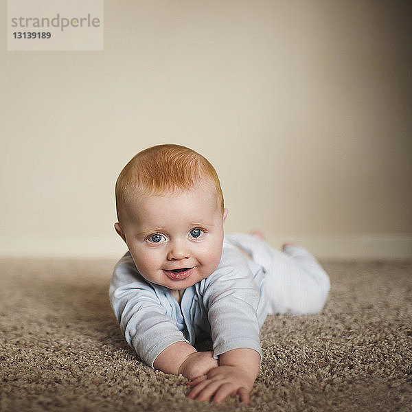 Porträt eines süßen kleinen Jungen  der zu Hause auf einem Teppich an der Wand liegt