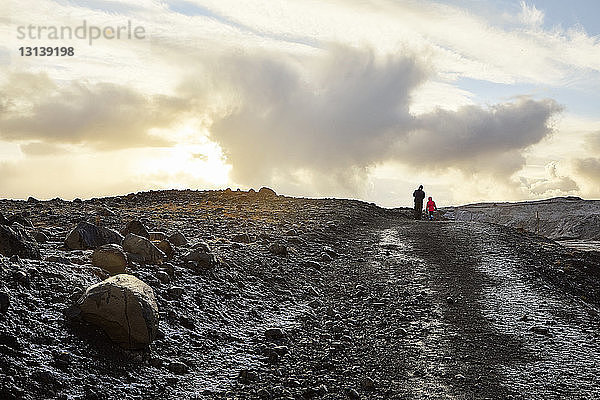 Rückansicht eines Vaters mit Tochter beim Spaziergang auf einem Berg vor bewölktem Himmel