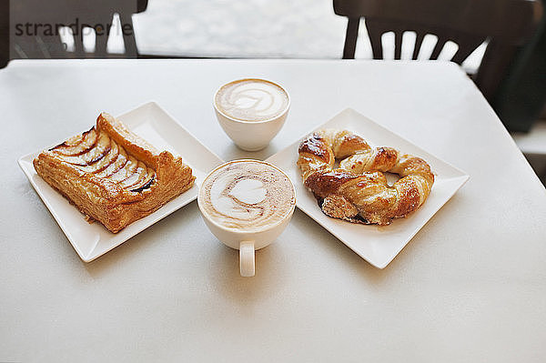Hochwinkelansicht von Cappuccino und Gebäck auf dem Tisch im Cafe